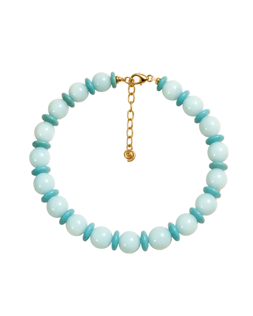 A beaded necklace displayed on a cream background with soft leaf shadows. The necklace features light aqua blue round beads alternating with smaller turquoise blue disc beads, finished with a gold clasp and extender chain.