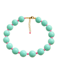 A beaded necklace with large mint green beads and small pink spacer beads, displayed on a beige background with decorative shadows. The necklace is labeled 'MIAMI POP NECKLACE' and 'SUMMER HEIRLOOMS' by the brand 'STACKED BY VALE'.