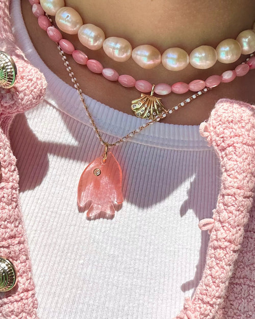 Close-up of a person wearing pink pearl necklaces and a pink textured cardigan.